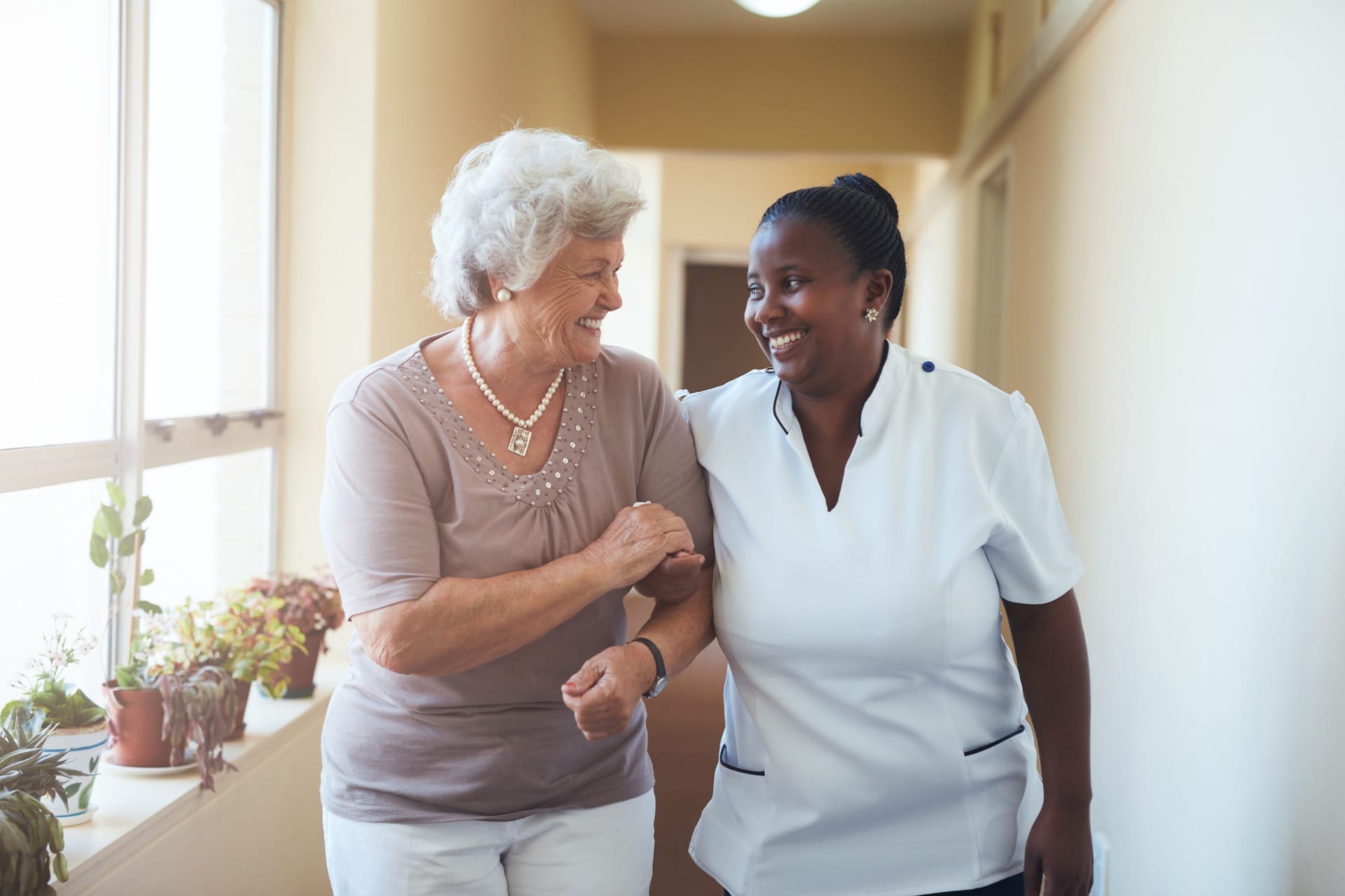 Elderly Woman And Caregiver Linked In Arms Smiling At Each Other