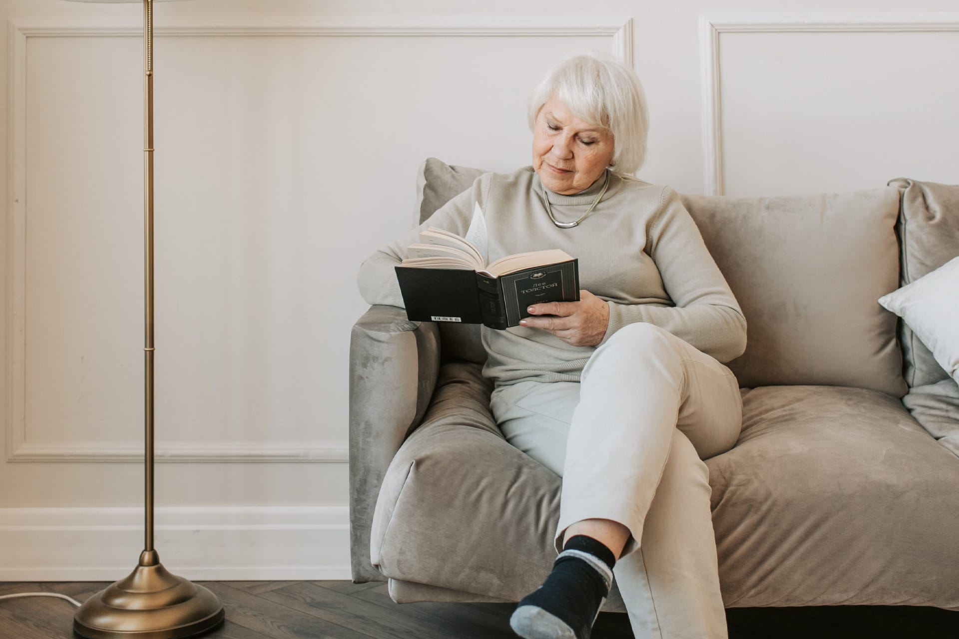 Elderly Woman Reading Book On Sofa